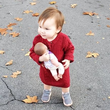 toddler in a red dress holding her baby doll like a godly parent